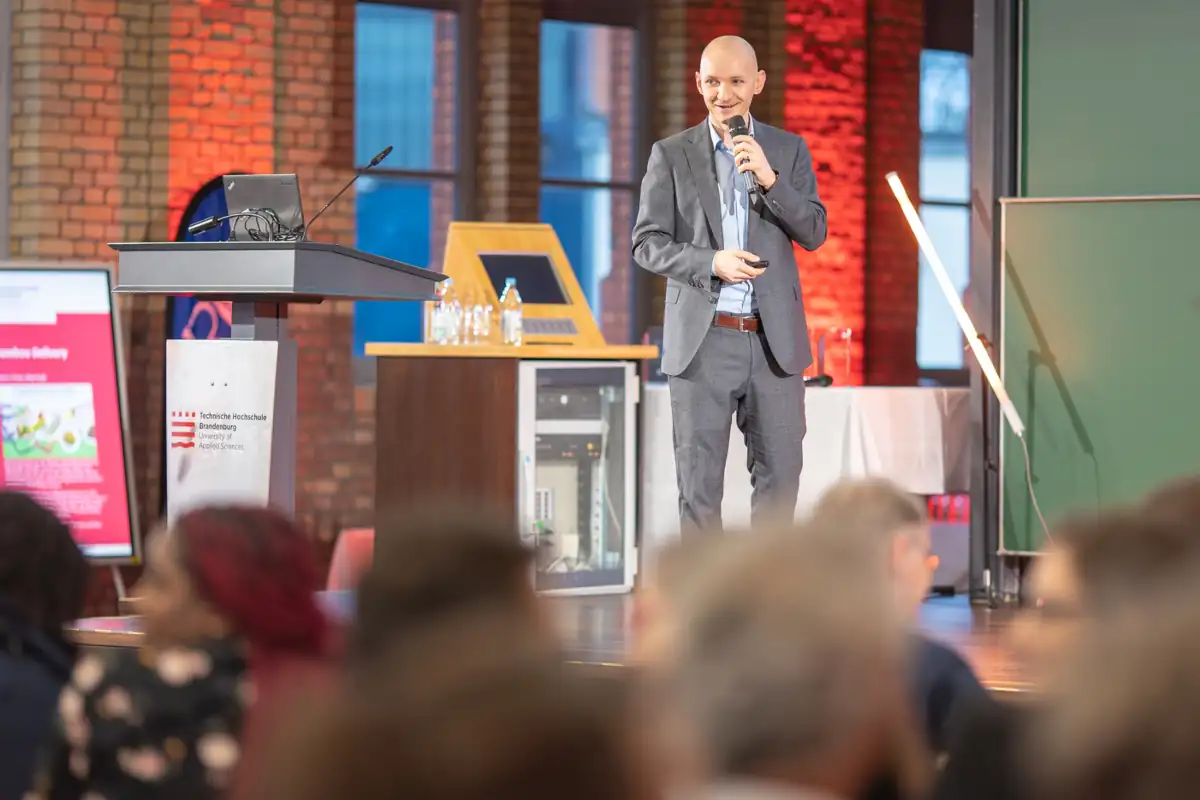 André Nitze präsentiert auf einer Bühne vor einem Publikum an der Technischen Hochschule Brandenburg
